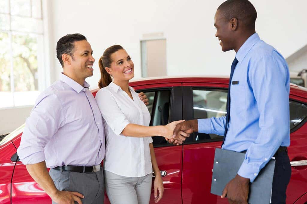 Couple shaking hands with car dealer