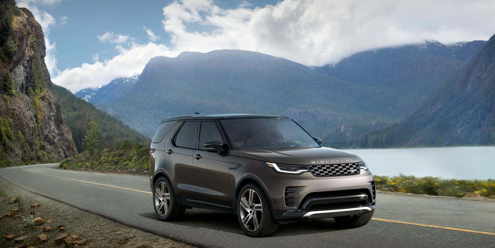 2024 land rover discovery on an open road with a lake and mountains in the background
