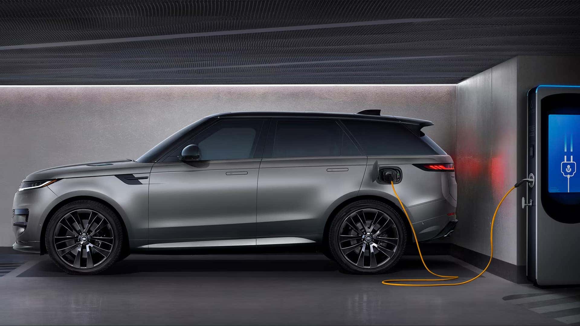 Silver Range Rover Sport plug-in hybrid model connected to charging station in modern garage
