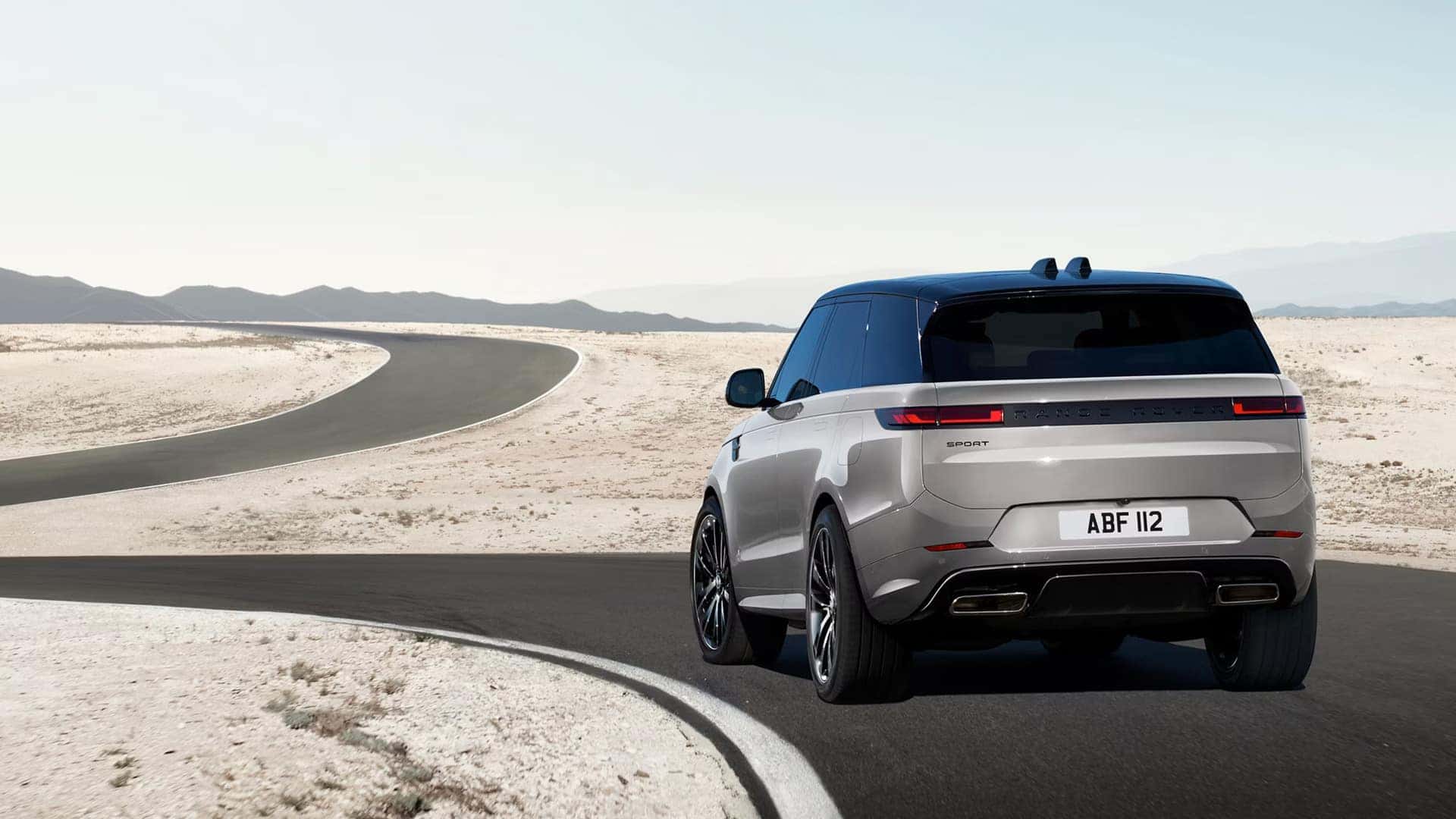 Rear view of silver Range Rover Sport driving on winding desert road showing taillight design