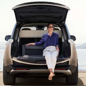 a woman sitting in the cargo space of a range rover with a body of water in the background