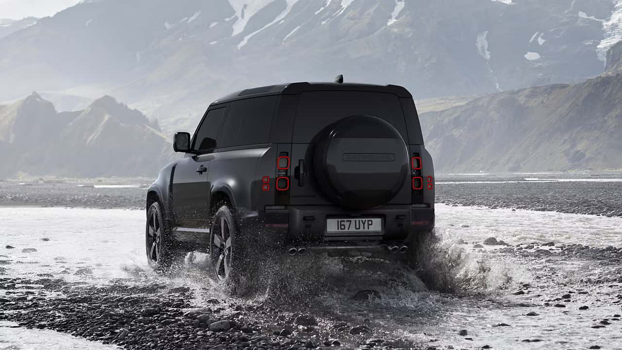 a black defender 90 driving in water with a rugged mountain terrain in the background