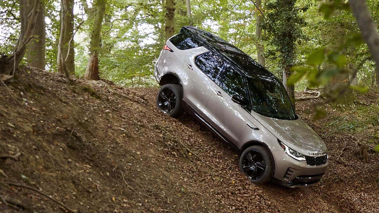 a 2026 land rover discovery going down hill in rugged forest terrain