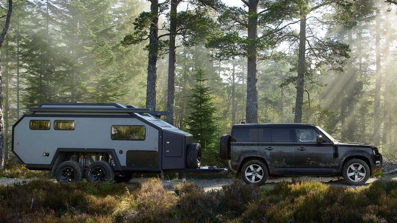a defender 110 driving in the woods with a camper trailer being pulled behind