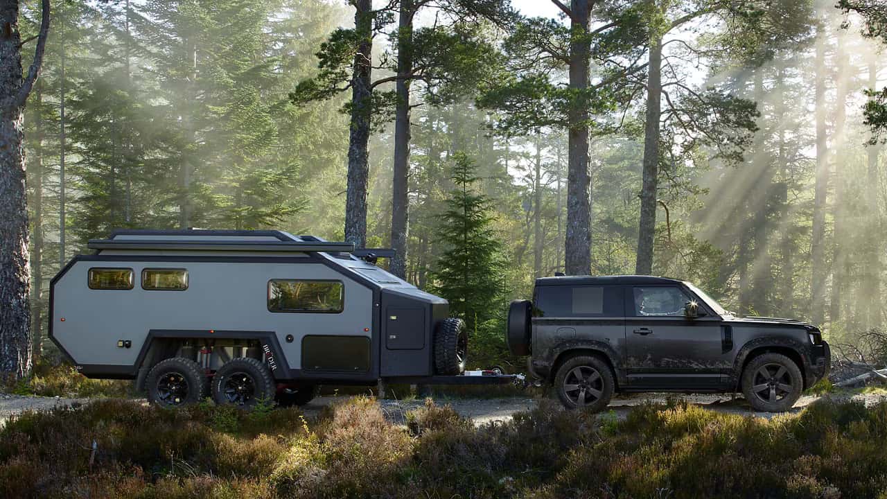 a 2026 defender 90 hauling a camper in the woods