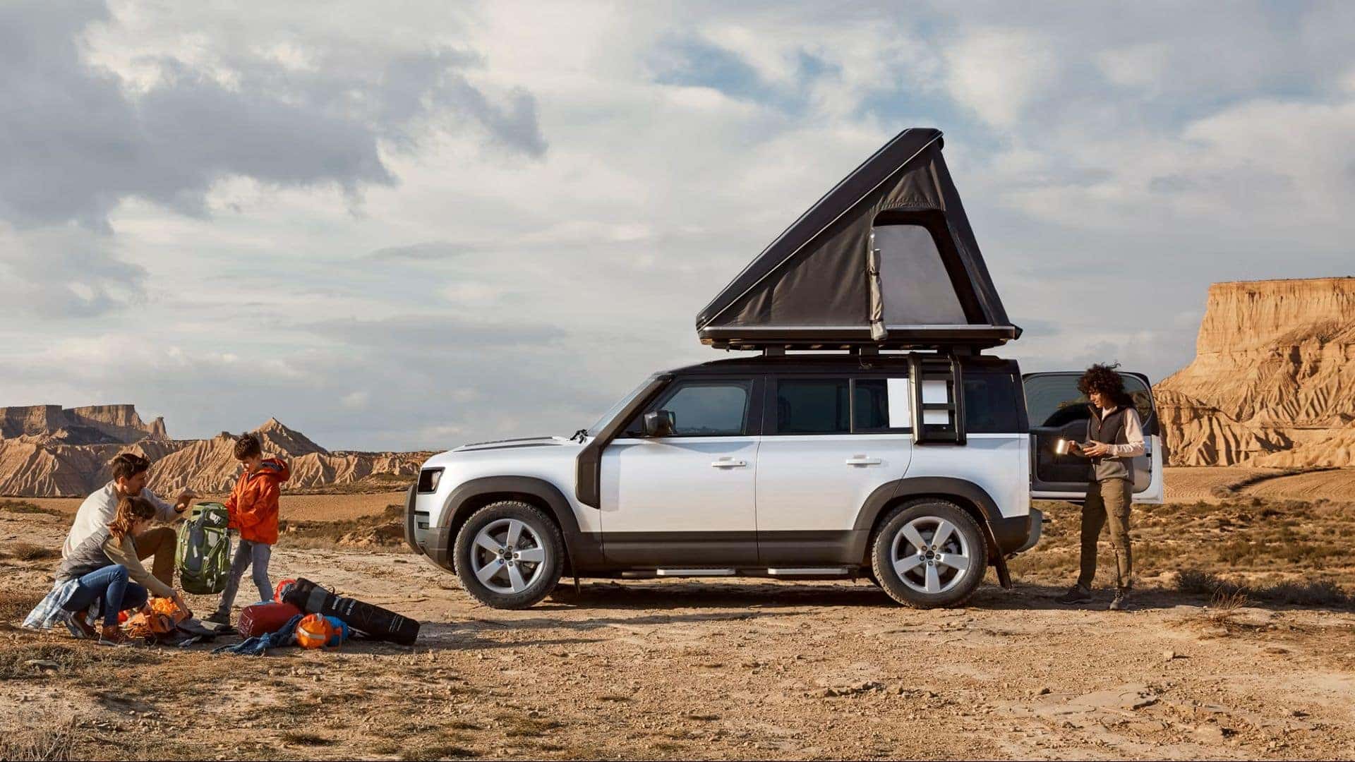 defender with a pop up camper on top of it and a family camping in the desert
