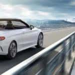 White C-Class Cabriolet driving up a highway with mountains in the background