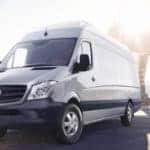 Gray Sprinter van parked in front of a bridge with a bright sunburst in the background