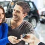 Now her dream comes true. Car salesman giving the key of the new car to the young attractive owners