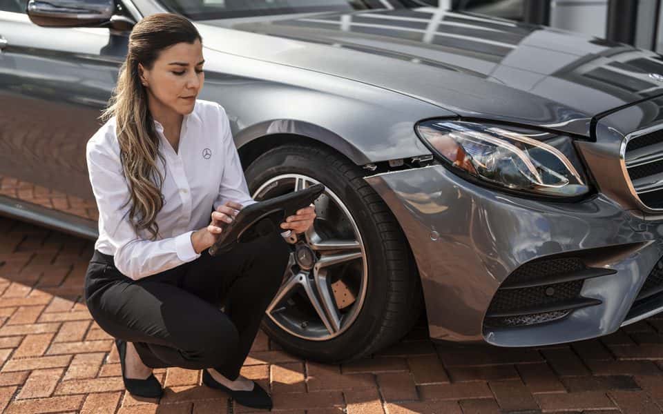 Mercedes-Benz advisor inspecting the front of a gray E-Class after a collision