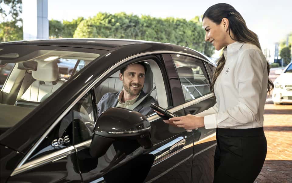 Mercedes-Benz Service Advisor with a tablet taking notes from a client seated in his Mercedes-Benz