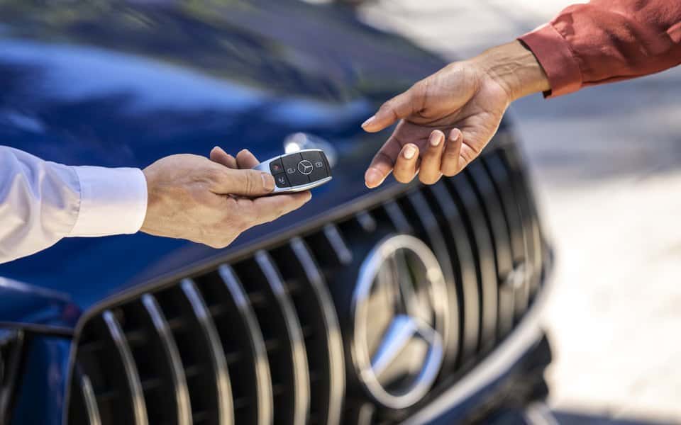 Mercedes-Benz key being handed over in front of a Mercedes-Benz grille and star