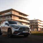 Silver Mercedes-Benz GLA compact SUV at sunset on a modern office campus, front three-quarter view with LED headlights and star grille.
