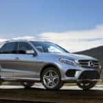 Silver Mercedes-Benz GLE parked in front of a building next to a lake with a bright sun in the background