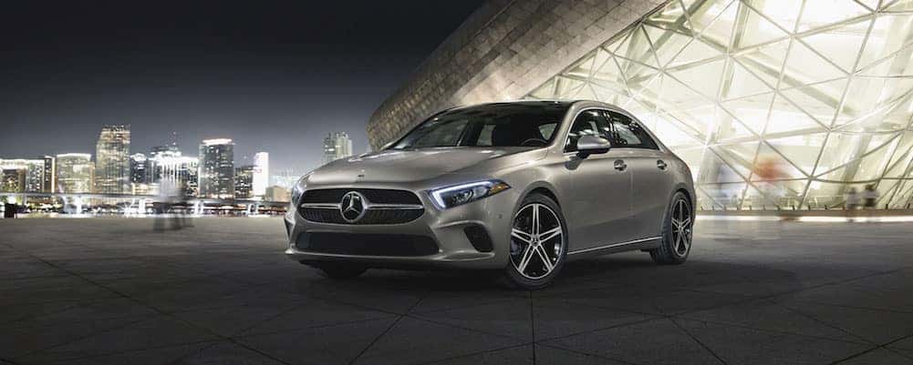 Silver A-Class sedan parked in front of a cityscape at night