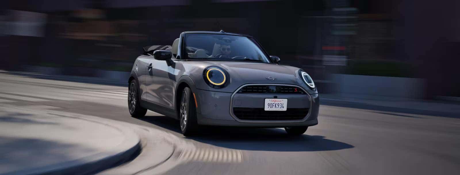 a man driving a 2026 mini cooper convertible through a round a bout. 