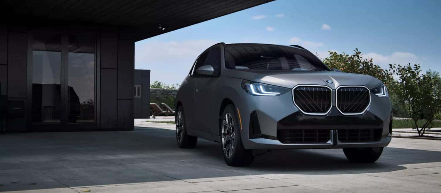 Front view of the 2025 BMW X3 parked in a modern driveway, showcasing its bold kidney grille and signature LED headlights.