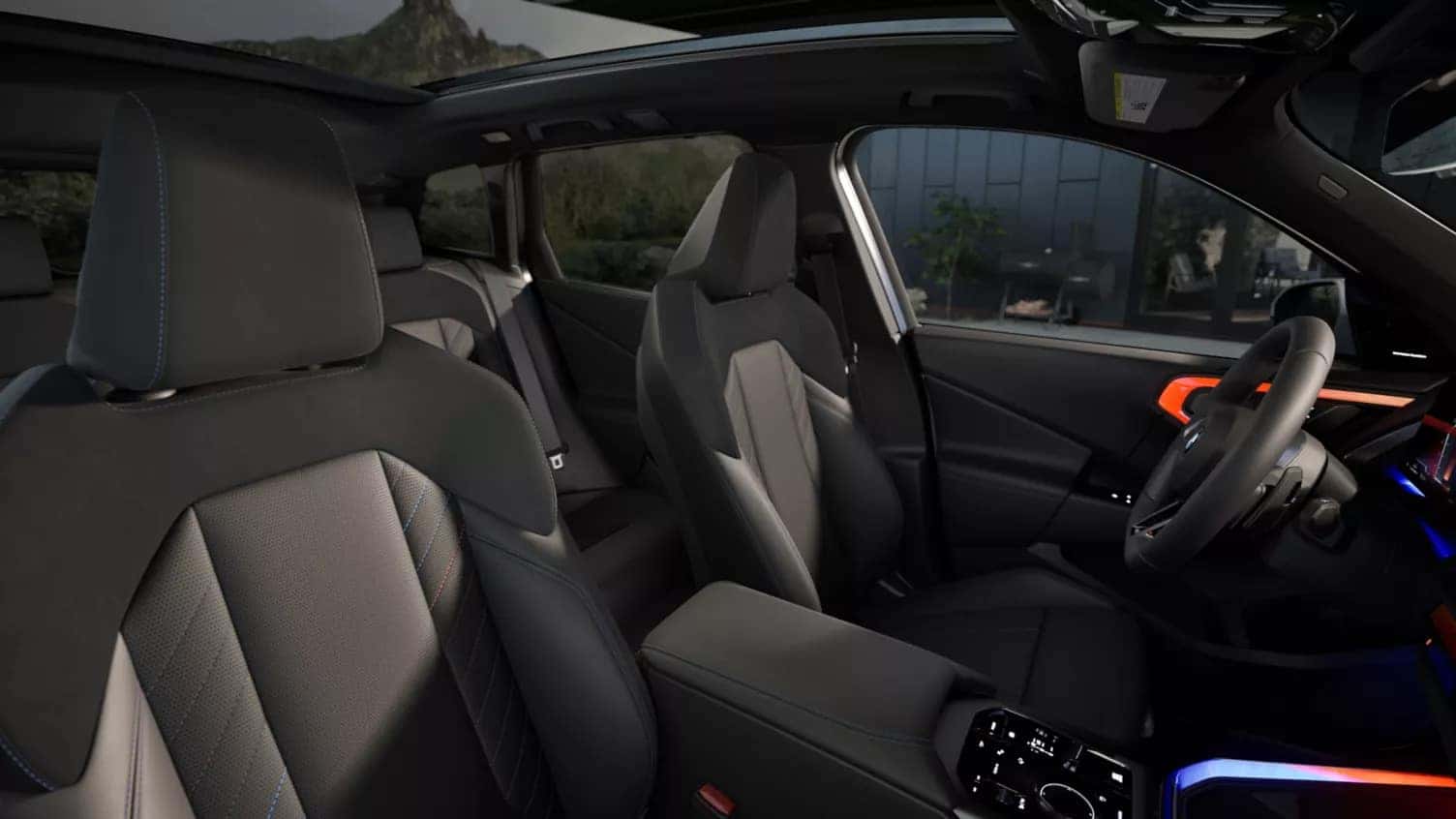 Interior view of the 2025 BMW X3 featuring black leather seats with contrast stitching, ambient lighting, and a panoramic sunroof.