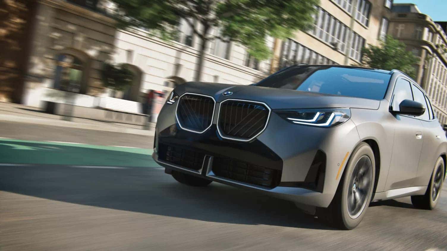 2025 BMW X3 driving through an urban cityscape, showcasing its bold grille, aerodynamic design, and LED headlights in motion.