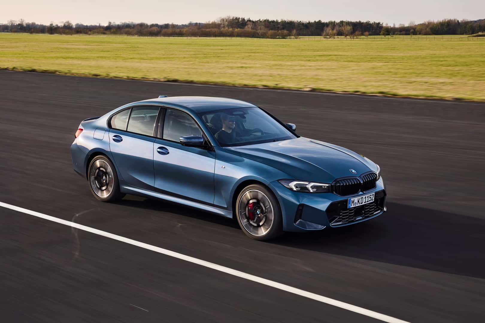 2025 BMW 330i Sedan in blue with black grille and M Sport wheels parked on pavement under a clear sky.
