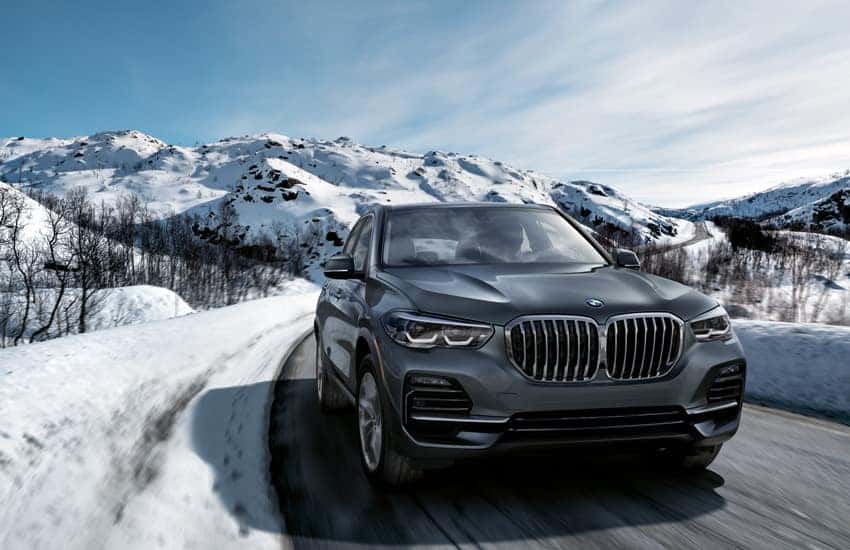 a bmw driving on a road with snow and snow capped mountains