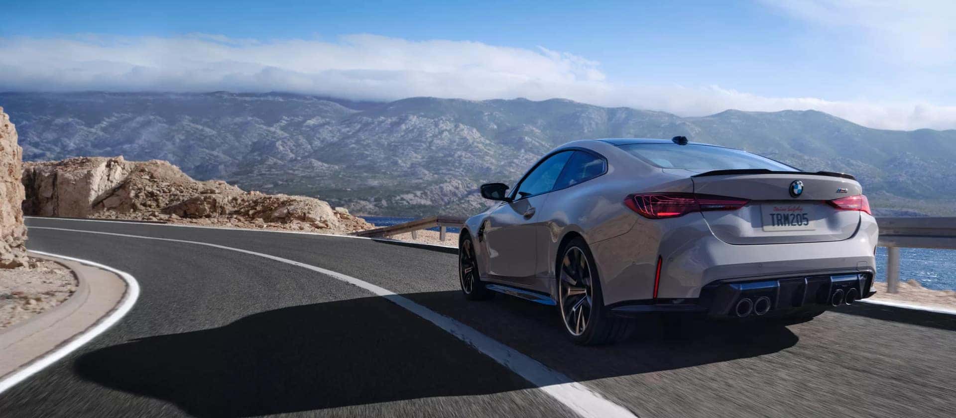 a grey 2026 BMW 4 Series driving down a road in the mountain range
