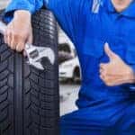 Technician with a blue workwear, holding a wrench and a tire while showing thumb up