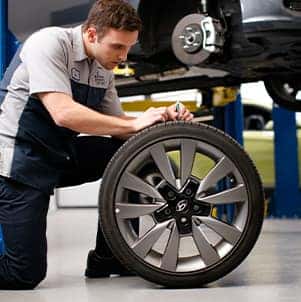 How to prepare your Hyundai for the winter season in Washington, PA at Washington Hyundai | Mechanic rolls in new tire for car thats on the lift